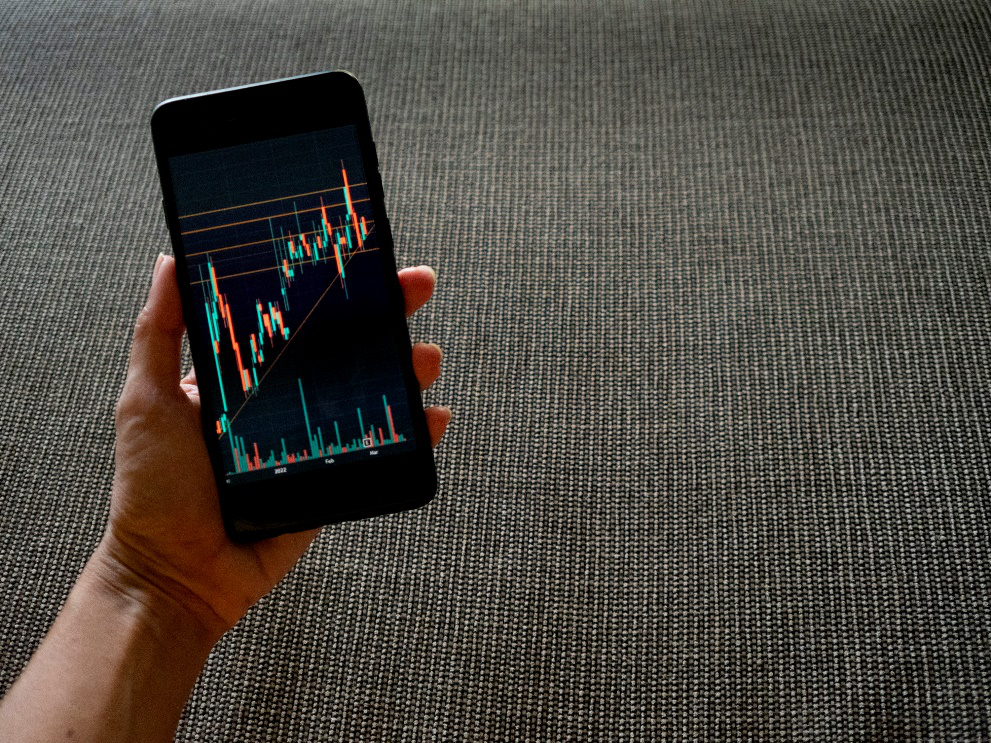 A person holding a cellphone with a trade chart on the screen